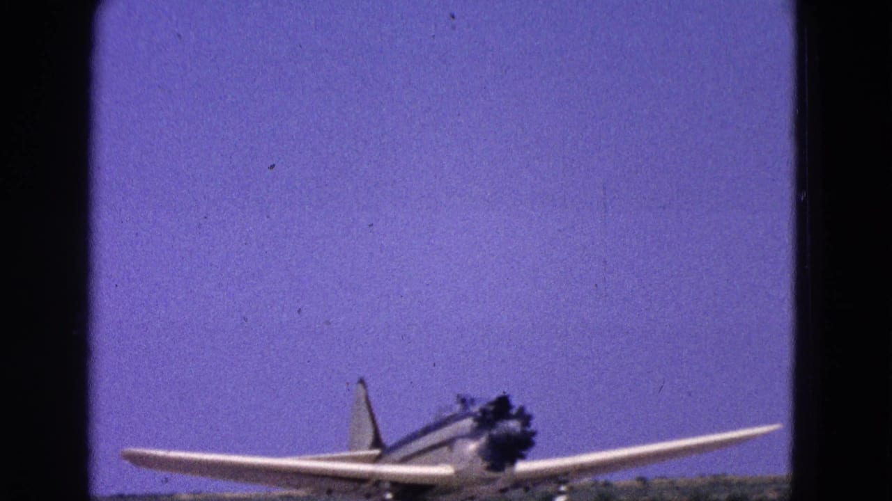 1964 Washington, DC home-movie frame showing a white single-engine propeller airplane with blue striping near the runway edge.