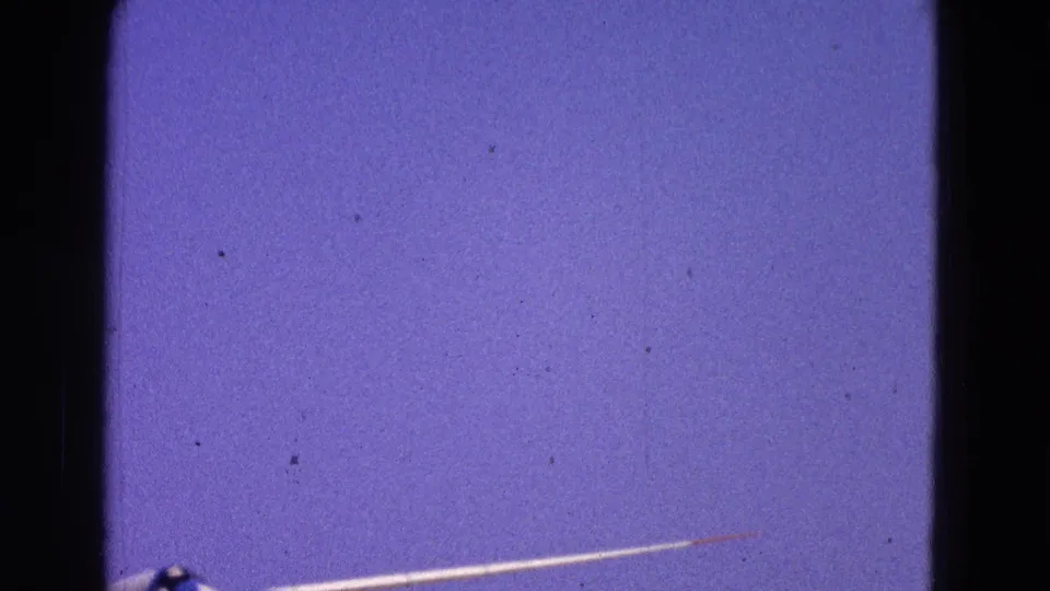 A white and blue glider begins to enter the 1964 8mm frame from below against a clear blue sky.
