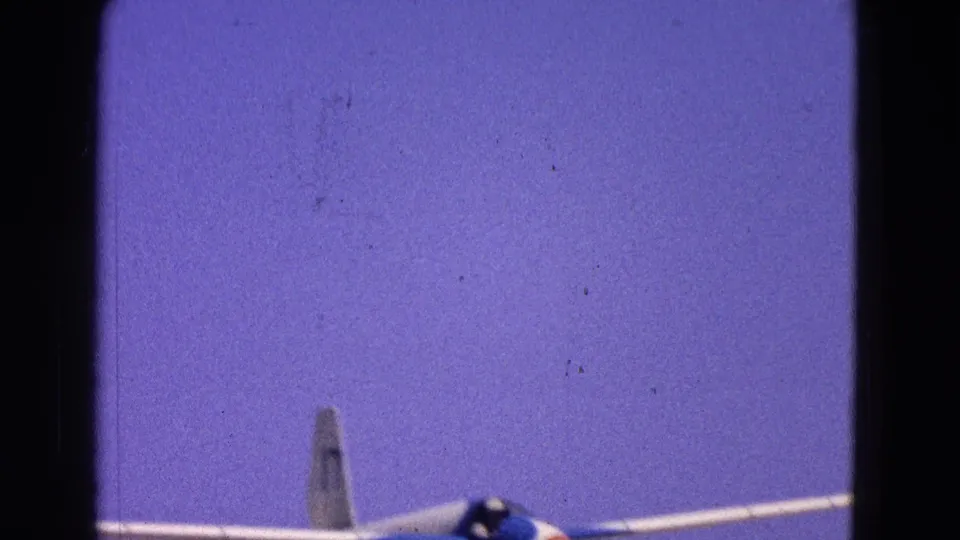 The blue and white glider climbs through the 1964 Washington DC home-movie frame with pilot visible in the cockpit.