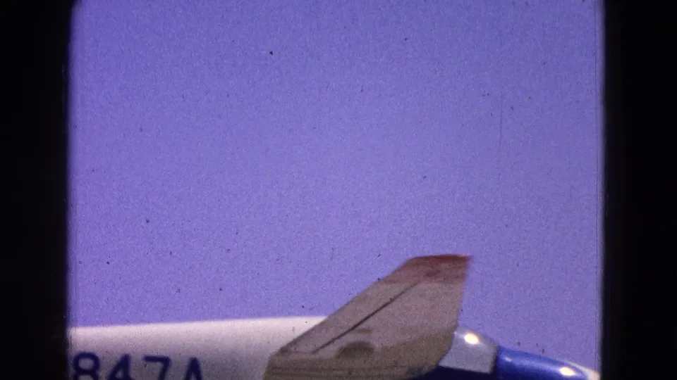 1964 Washington, DC home-movie frame showing part of a blue and white airplane and registration markings against a pale sky.