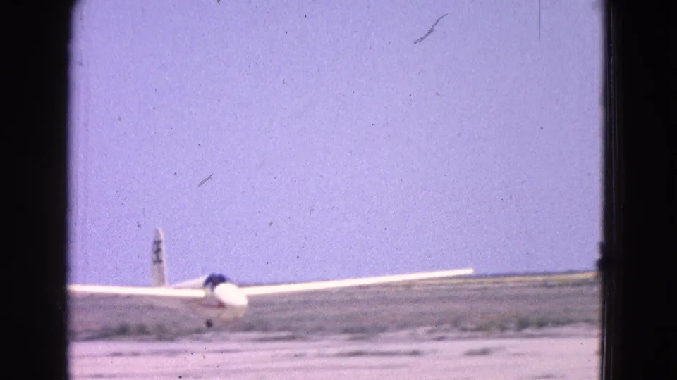 1964 Washington DC home-movie frame showing a small white aircraft near the runway, partly obscured by dark framing and film wear.