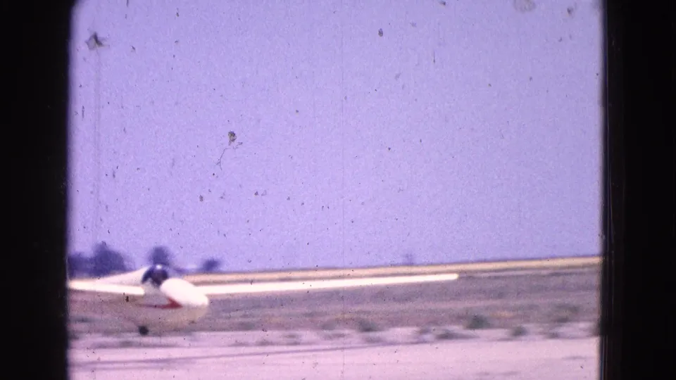 1964 Washington DC archival frame showing a small white glider or light plane rising from a flat airfield under a bright sky.
