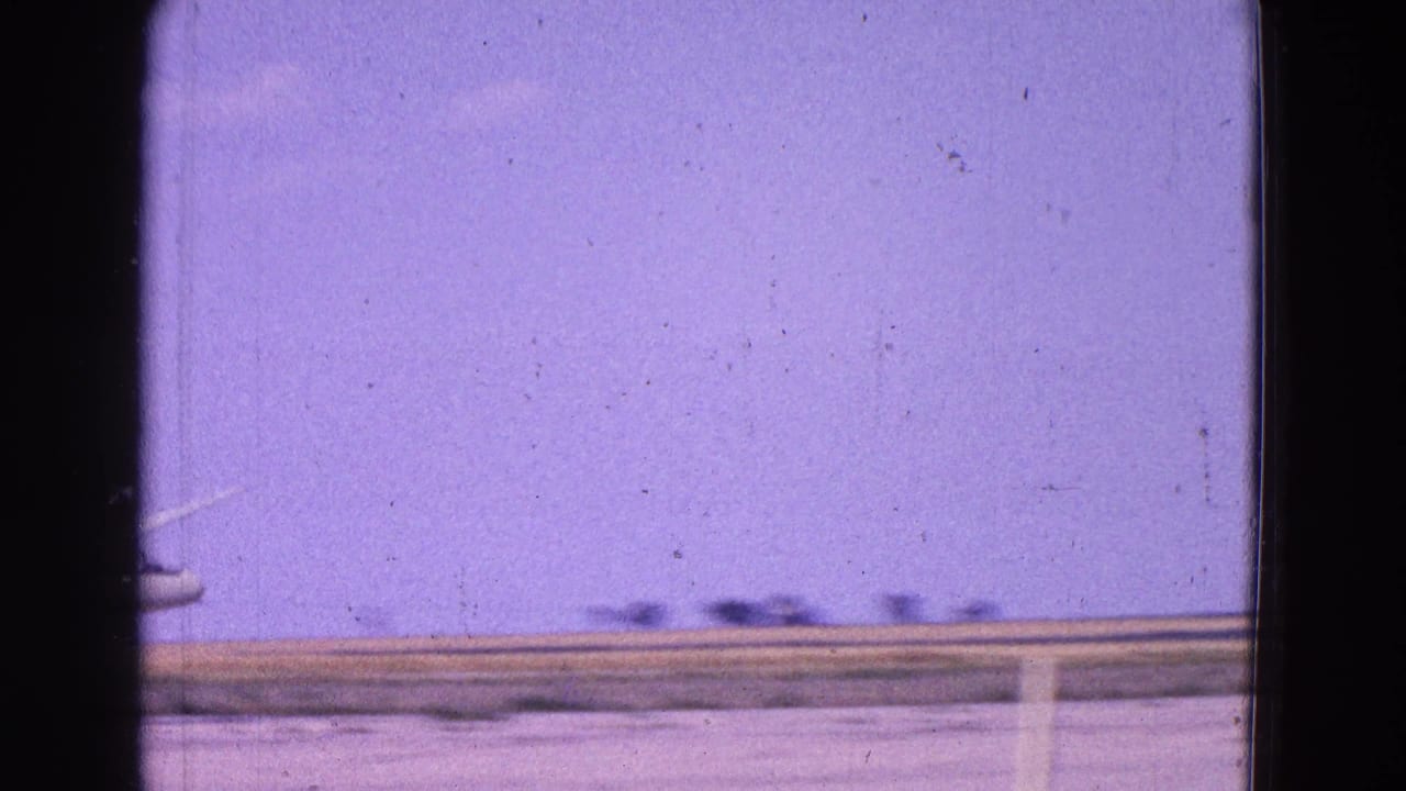 Small plane near a flat horizon beneath a purple sky, framed by dark 8mm film borders.