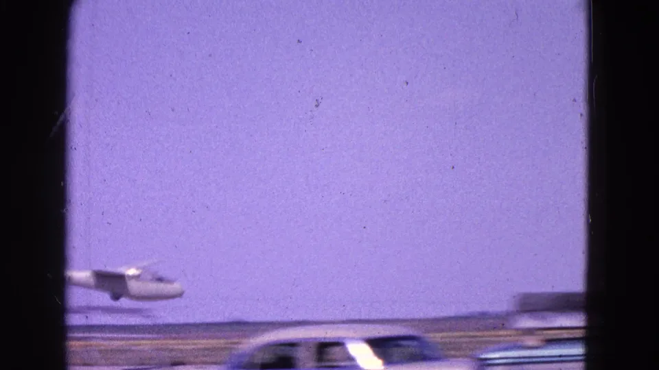 1964 Washington, DC area 8mm frame showing a small plane approaching low while a car passes near the bottom edge.