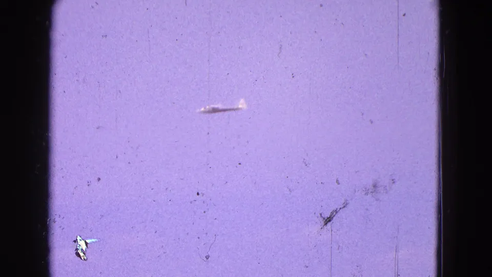 1964 Washington, DC area 8mm frame with a small plane isolated against a hazy purple sky and visible film wear.