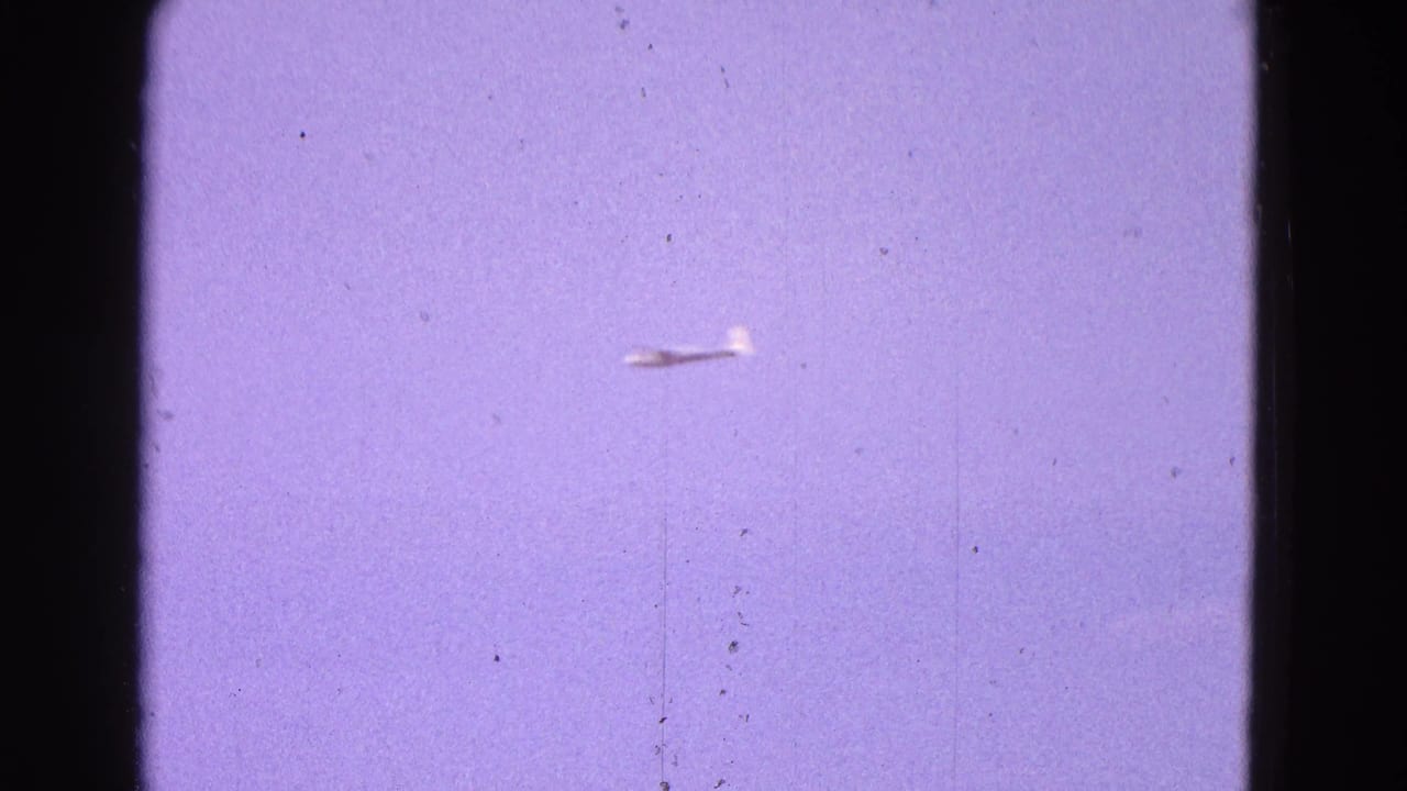 Distant white glider flying through blue sky in 1964 Washington, DC home-movie footage.