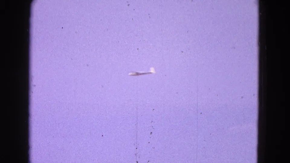 Distant white glider flying through blue sky in 1964 Washington, DC home-movie footage.