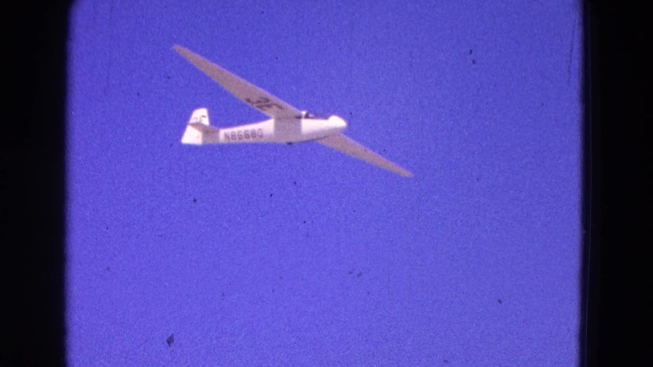 White glider with visible registration markings crosses a deep blue sky in 1964 Washington, DC footage.