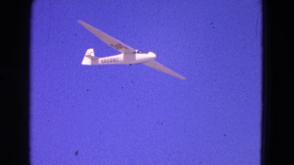 White glider with visible registration markings crosses a deep blue sky in 1964 Washington, DC footage.