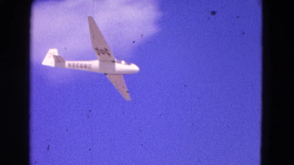 White glider marked N86680 banks near a small cloud in 1964 Washington, DC home-movie footage.