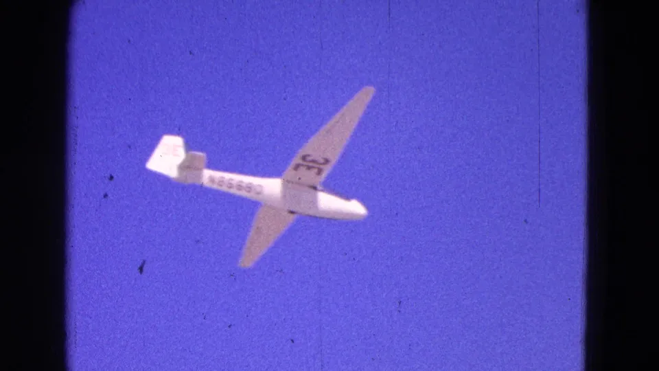 White glider with N86680 on the fuselage banks through blue sky in 1964 Washington, DC footage.