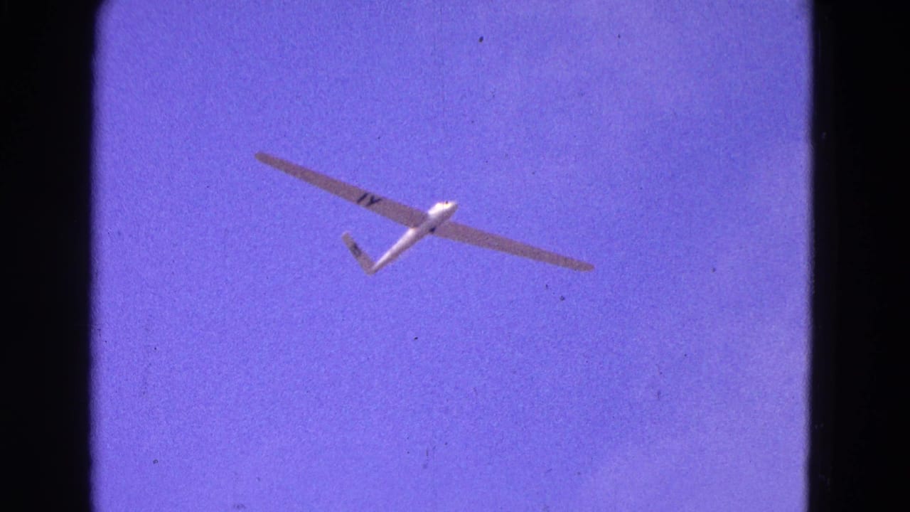 1964 Washington, DC 8mm frame showing a white glider with 1Y-style markings crossing a purple-tinted sky.