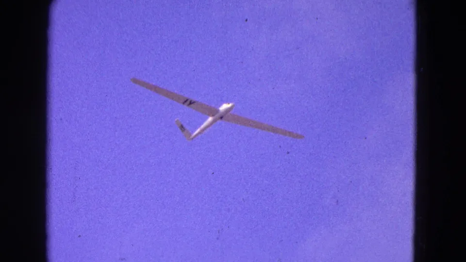 1964 Washington, DC 8mm frame showing a white glider with 1Y-style markings crossing a purple-tinted sky.