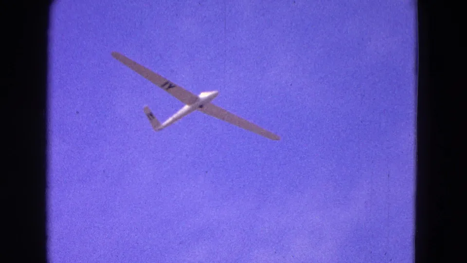 The glider appears higher in frame, its long wings and dark markings visible against the saturated 8mm sky.