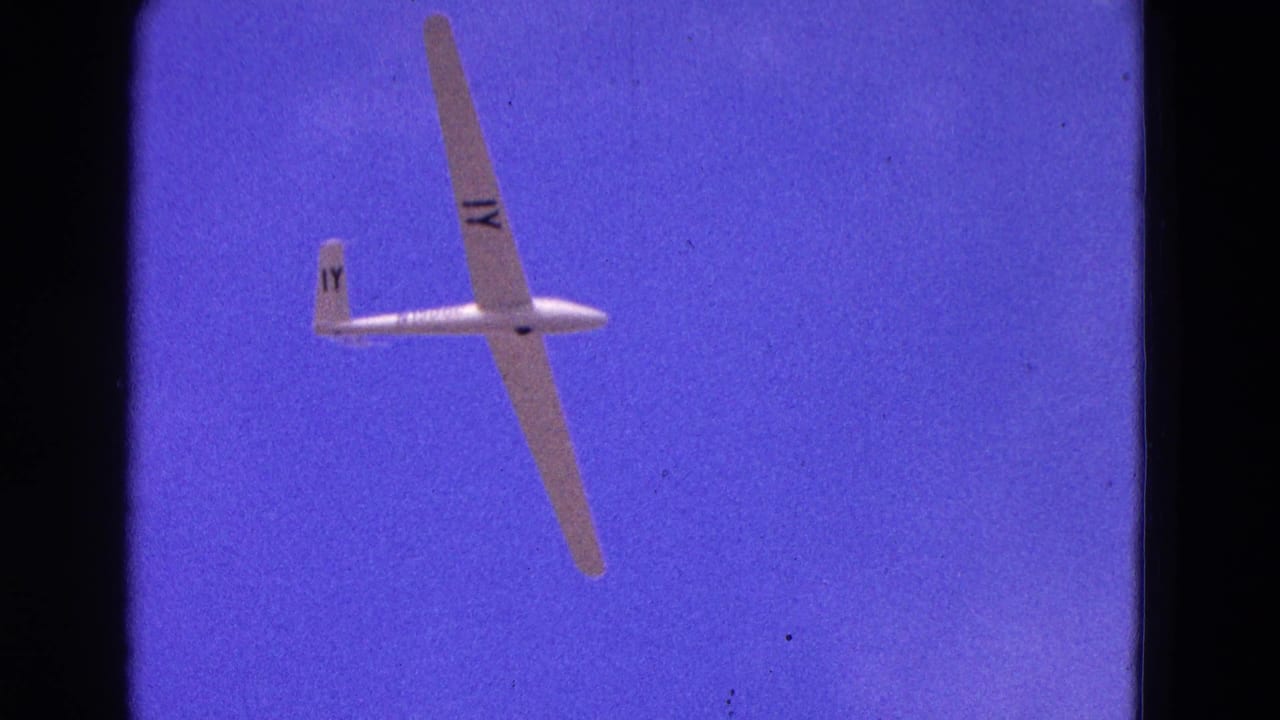 White glider banking against a deep blue sky with black film borders.