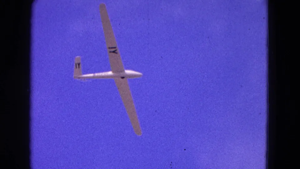 1964 home-movie frame of a white glider seen from below against a saturated blue sky in the Washington, DC clip context.
