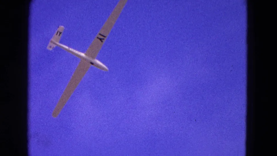 A white glider banks diagonally through the blue sky, captured in saturated 8mm color during the 1964 Washington, DC clip.