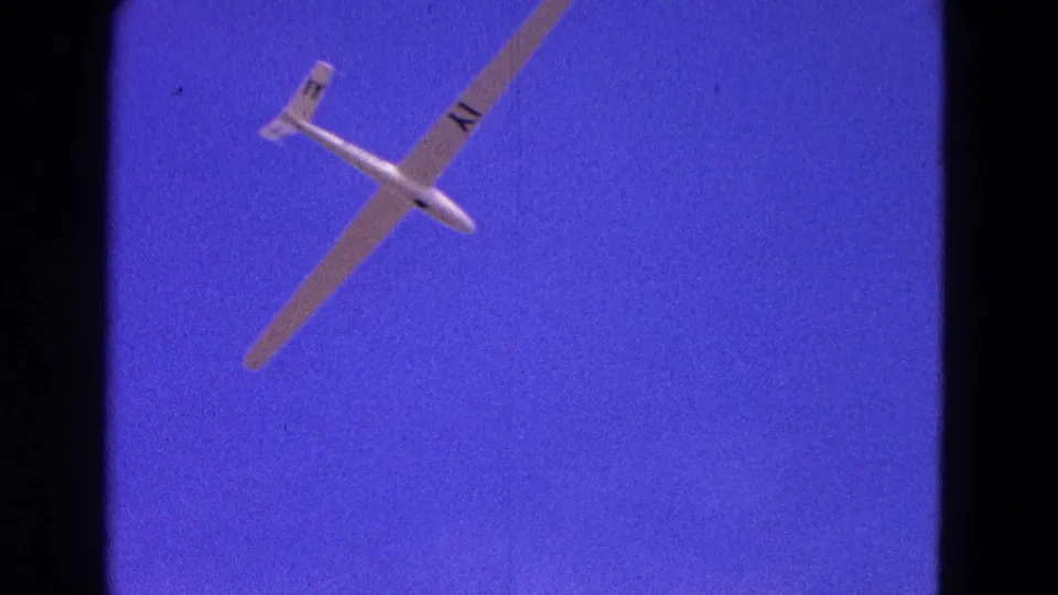 Final frame view of the white glider tilted across saturated blue sky, with 8mm grain and frame borders visible.