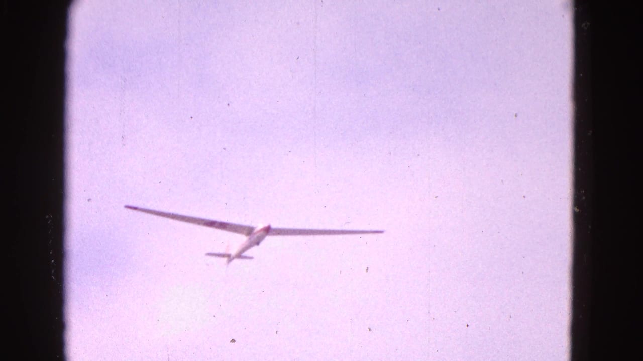 Distant white glider seen from below in pale sky with long wings spread wide.
