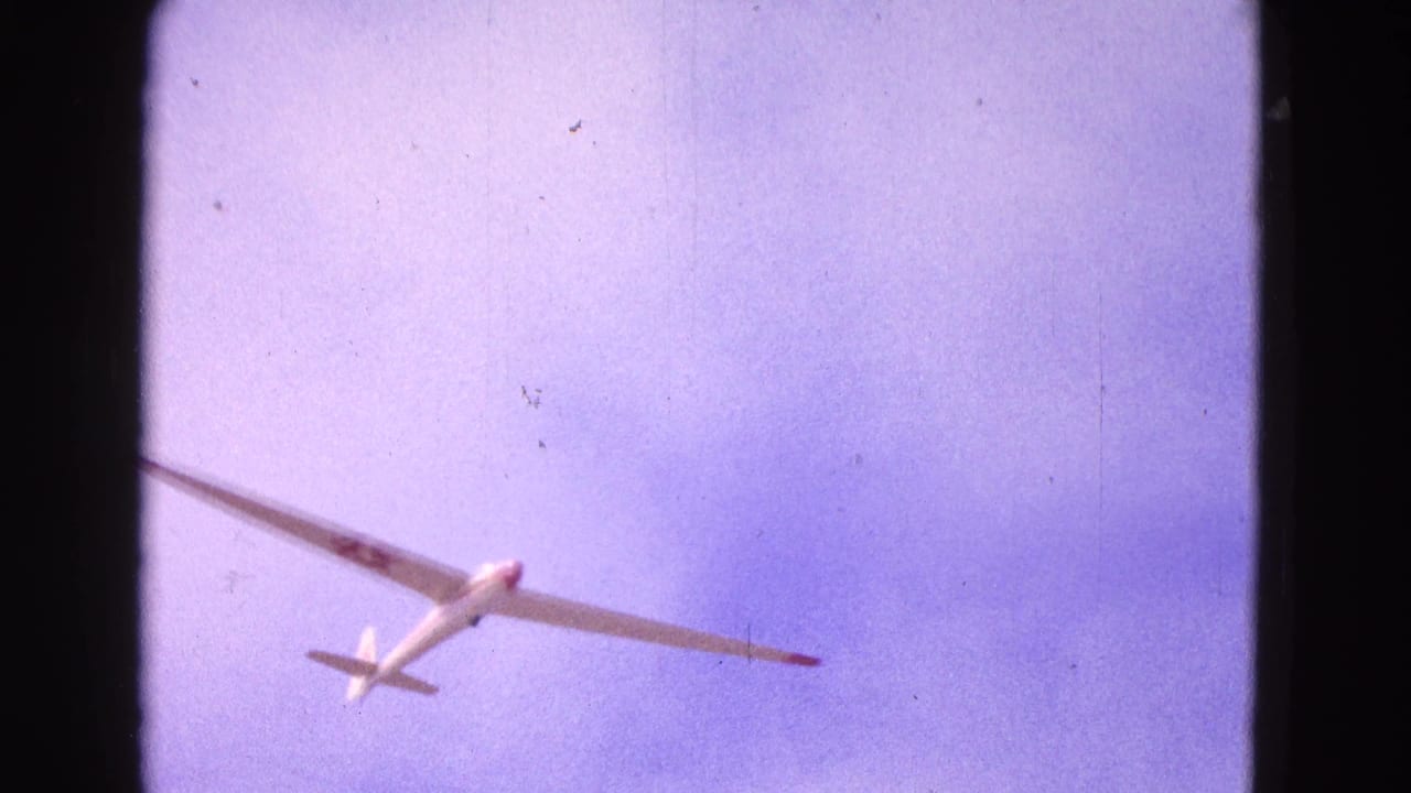 1964 Washington, DC 8mm frame showing a white glider banking across a purple-blue sky with film gate edges visible.