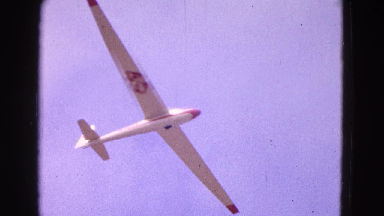 White glider banking in a pale blue sky with red wing tips and wing number 45.