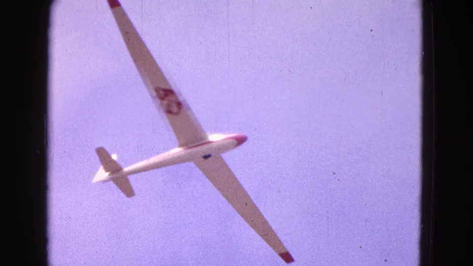 1964 8mm frame of a white glider with red accents and number 45 banking over Washington, DC sky.