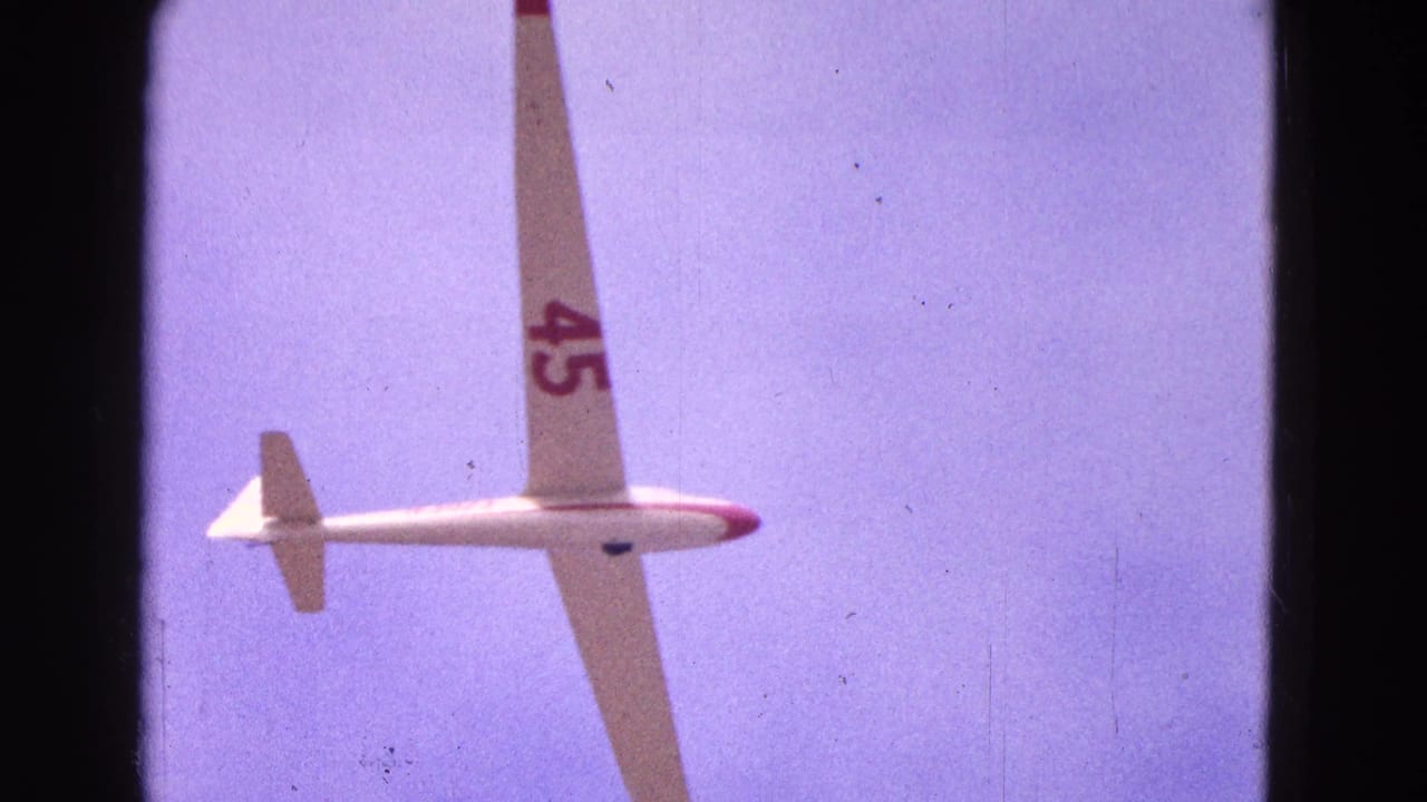 The glider passes overhead in the 1964 home-movie frame, showing its long wing and number 45 against blue sky.