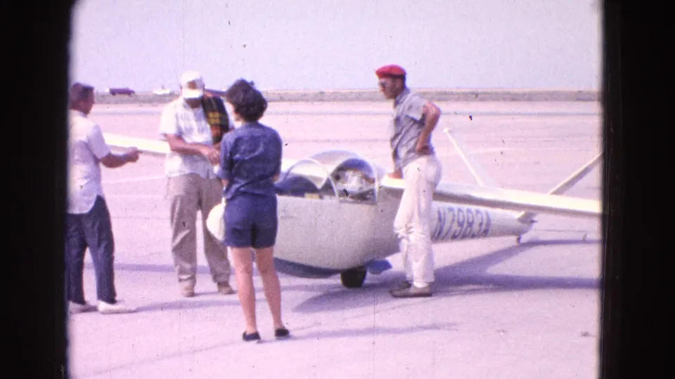 A small group stands beside the same white glider on the Washington, DC airfield, with aircraft markings visible near the fuselage.