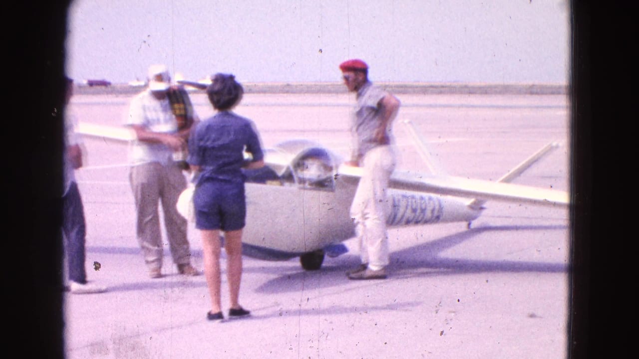 People standing around a small white glider on an airfield.