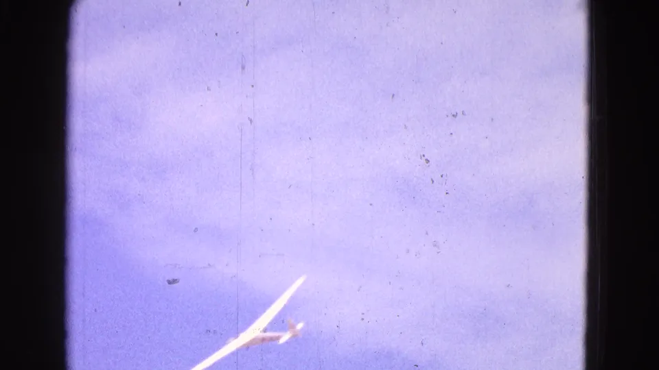 1964 8mm still with a white glider angled upward near the lower frame edge over Washington, DC, with purple-blue color shift.