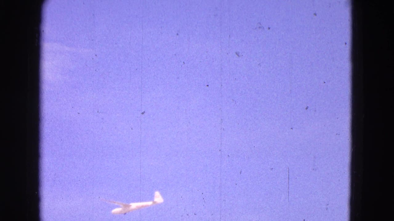1964 8mm frame from Washington, DC showing a small white glider against a purple-blue sky with visible film texture.
