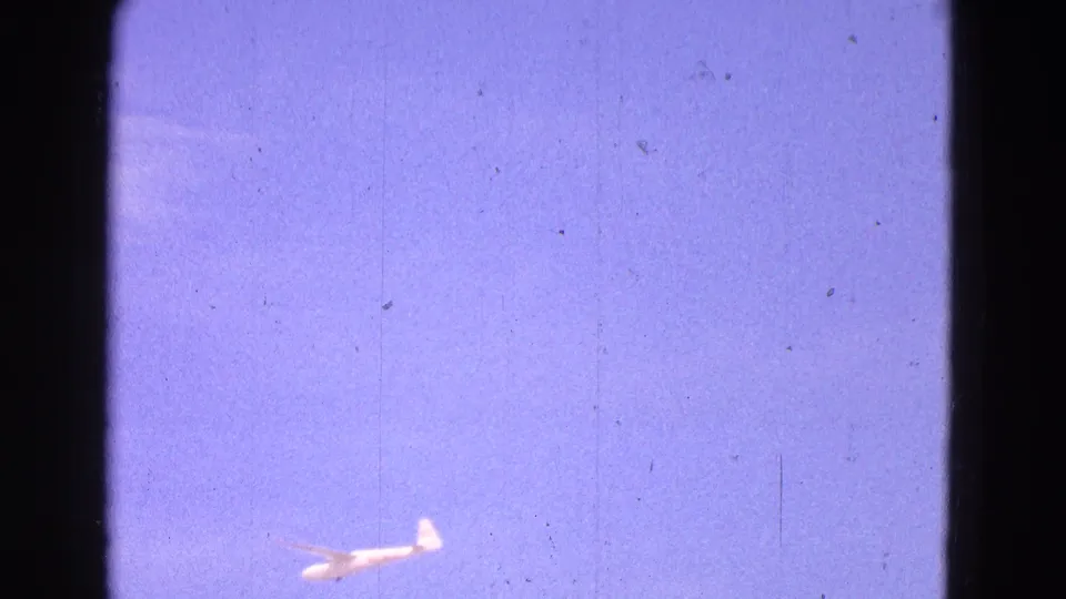 1964 8mm frame from Washington, DC showing a small white glider against a purple-blue sky with visible film texture.