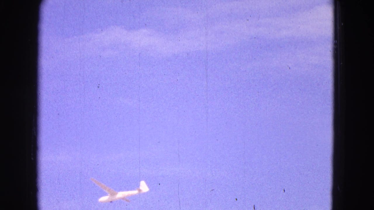 Small glider centered low in a purple-blue sky with scratches and dust marks.