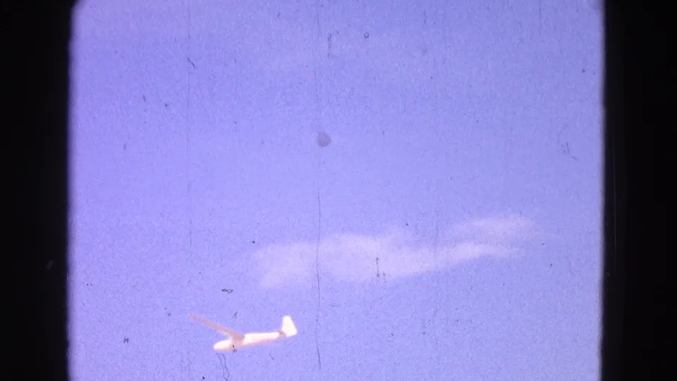 Final 1964 8mm frame showing the glider against a hazy purple-blue sky with visible scratches and dust.