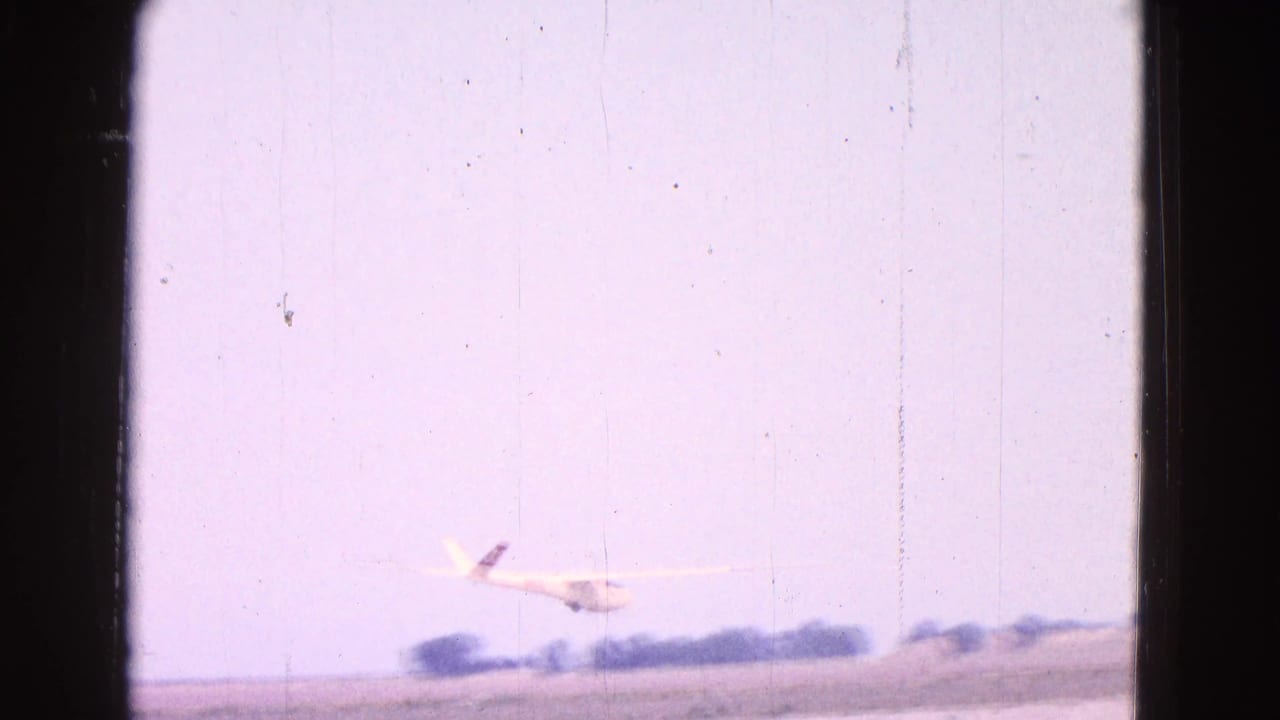 Small white glider near a rural runway with trees on the horizon and 8mm borders.