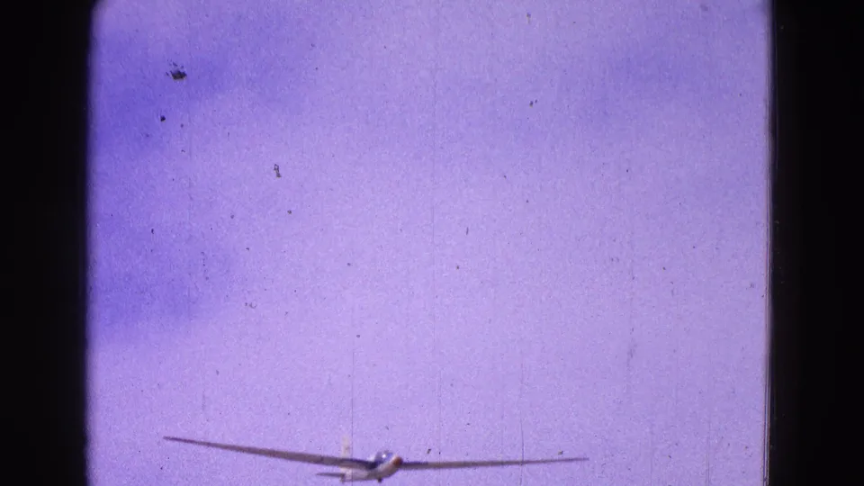The glider is airborne against a faded pale sky, seen from a distance in a soft 1964 8mm home-movie frame.