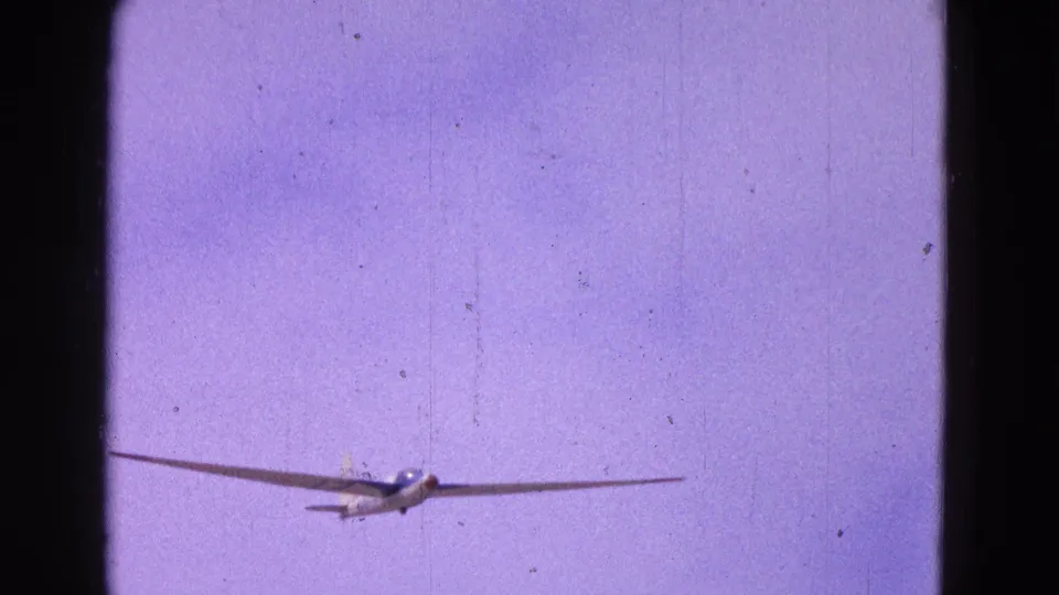 A small glider flies toward the camera in the 1964 Washington, DC-area home movie, framed by visible 8mm gate edges.