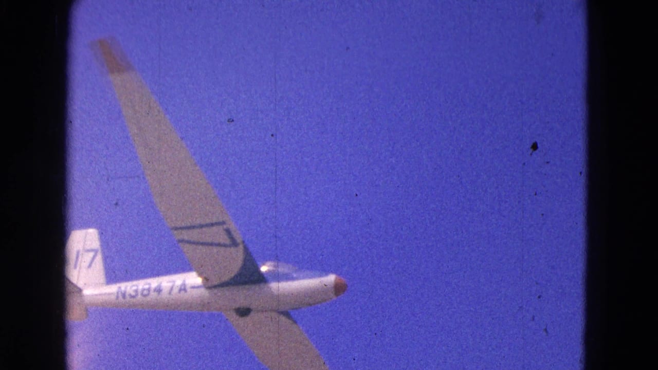 White glider with long wings and tail number 17 seen in flight against blue sky.