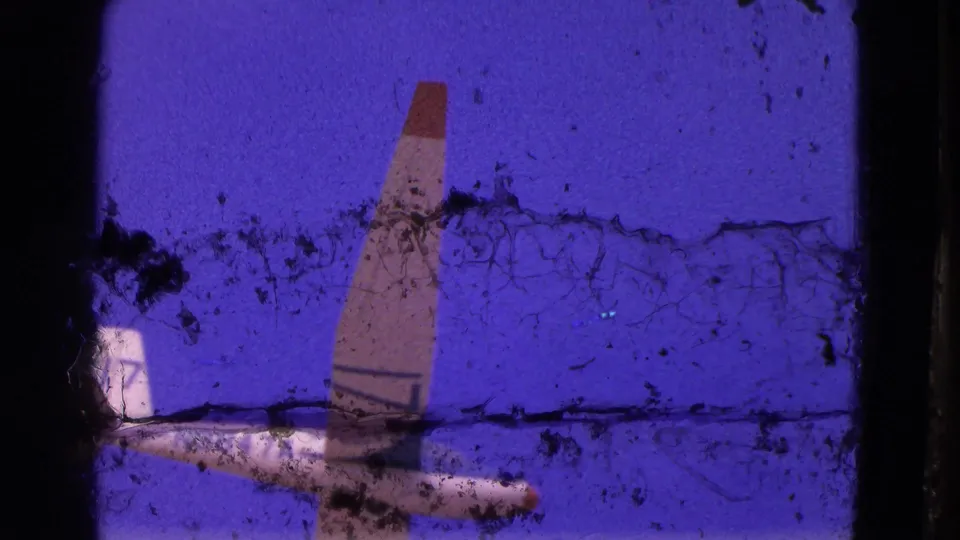 A glider tail and fuselage appear near the edge of the 1964 8mm frame, with heavy dust and emulsion marks across the sky.