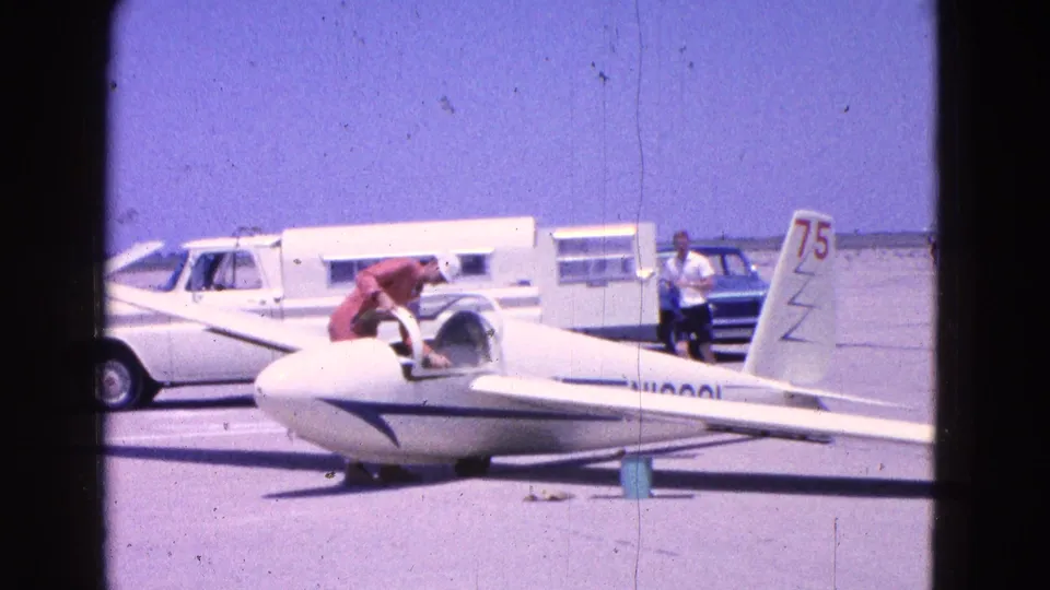 At the Washington, D.C. airfield, a white glider marked 75 sits on the tarmac as a man in red works near the cockpit.