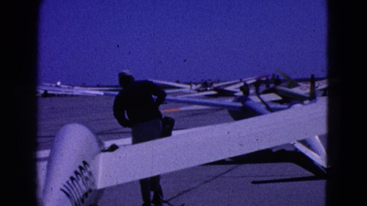Washington DC 1964 8mm frame showing a man inspecting or standing beside a glider wing with parked gliders across the tarmac.