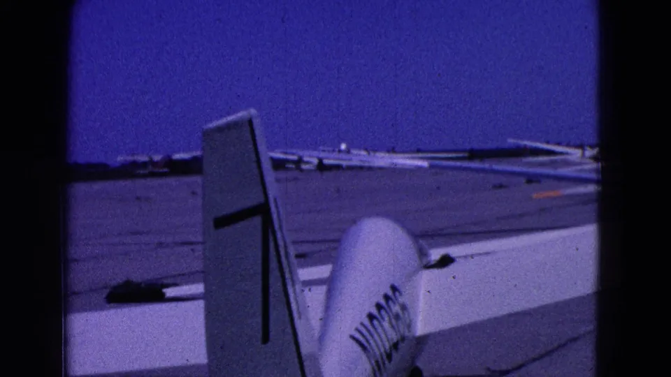 1964 Washington, DC-area 8mm frame showing the tail of a small white aircraft on a tarmac with distant light planes.