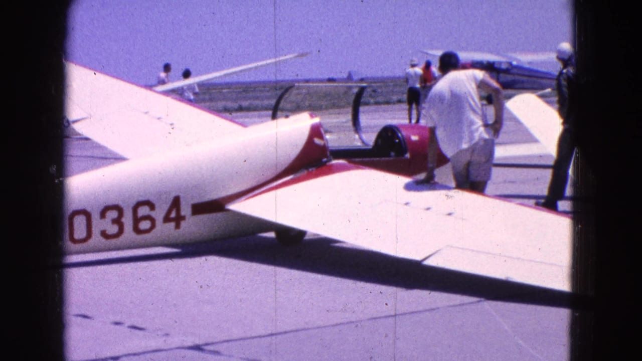 A white and red glider marked 0364 sits on the tarmac as men stand nearby in casual clothing.
