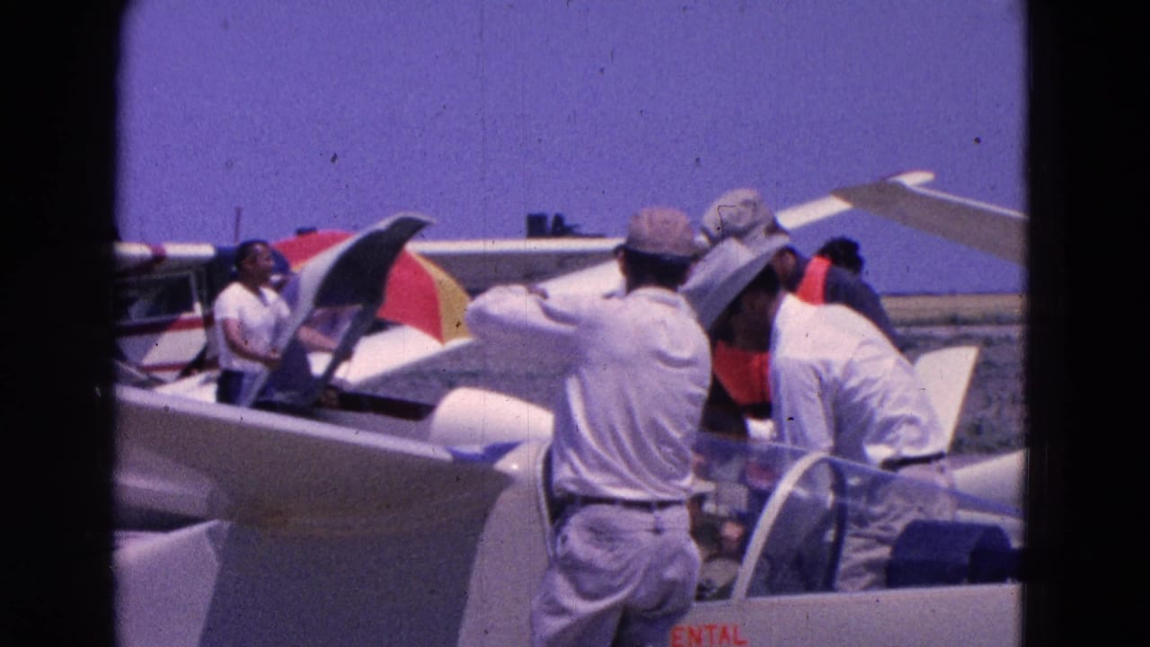 Men gather beside white gliders and open canopies at a sunny airfield.