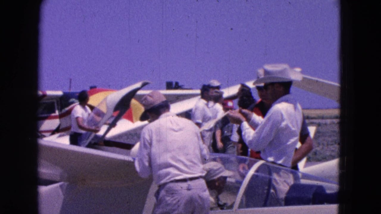 Men at a Washington DC airfield in 1964 appear to confer beside gliders and a small plane under a clear sky.