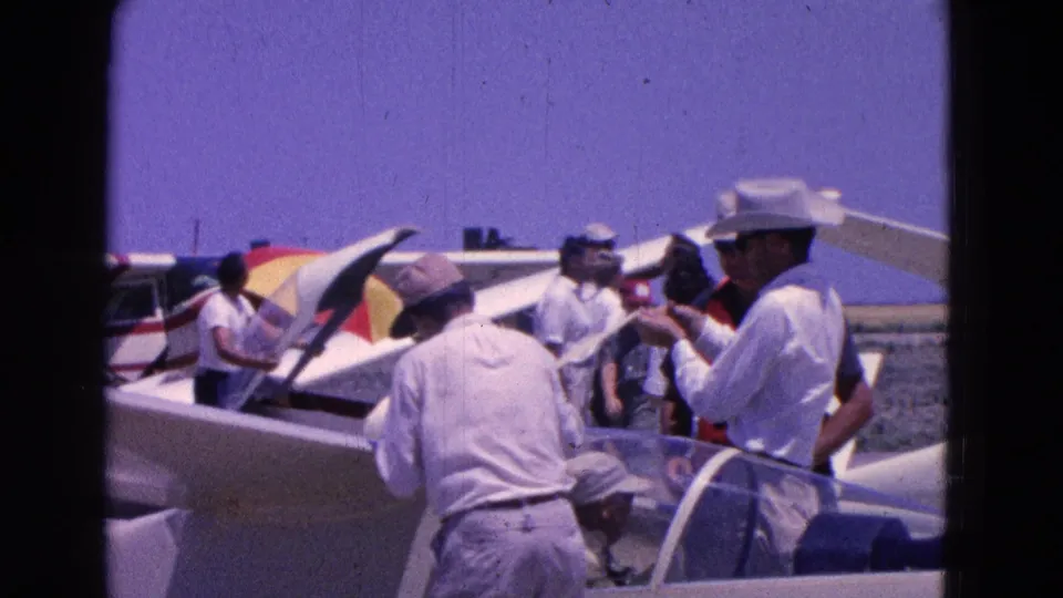 Men at a Washington DC airfield in 1964 appear to confer beside gliders and a small plane under a clear sky.
