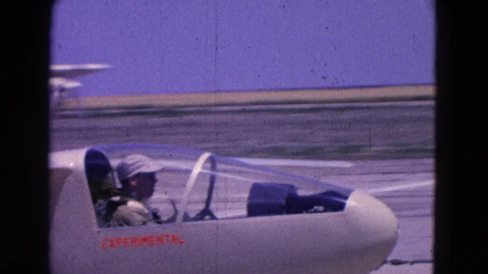 White experimental glider with a seated pilot moves or rests on a Washington DC airfield runway in 1964 footage.