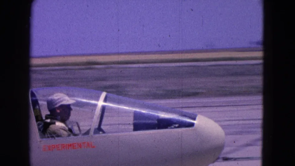 1964 8mm frame showing a pilot seated in a small experimental aircraft on a Washington DC runway.