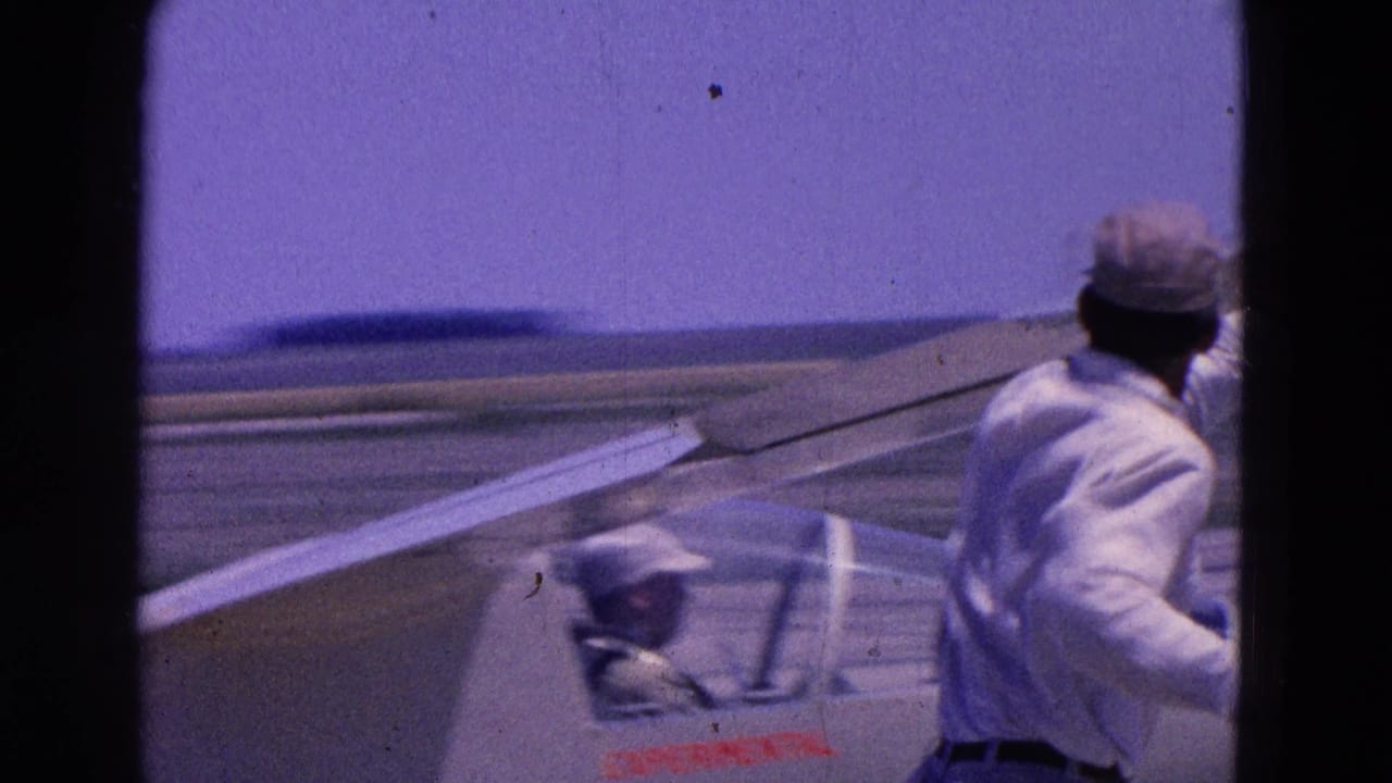A man in a light shirt and cap runs near the wing of the small experimental aircraft on a runway.