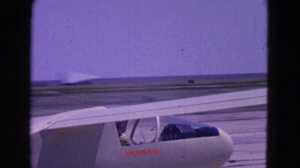 The small experimental aircraft is seen from the side with its long wing spanning the frame on the runway.